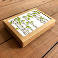 Load image into Gallery viewer, A square kraft paper gift box with a clear window showing a white card printed with a birch or aspen tree illustration, placed on a rustic wooden surface.