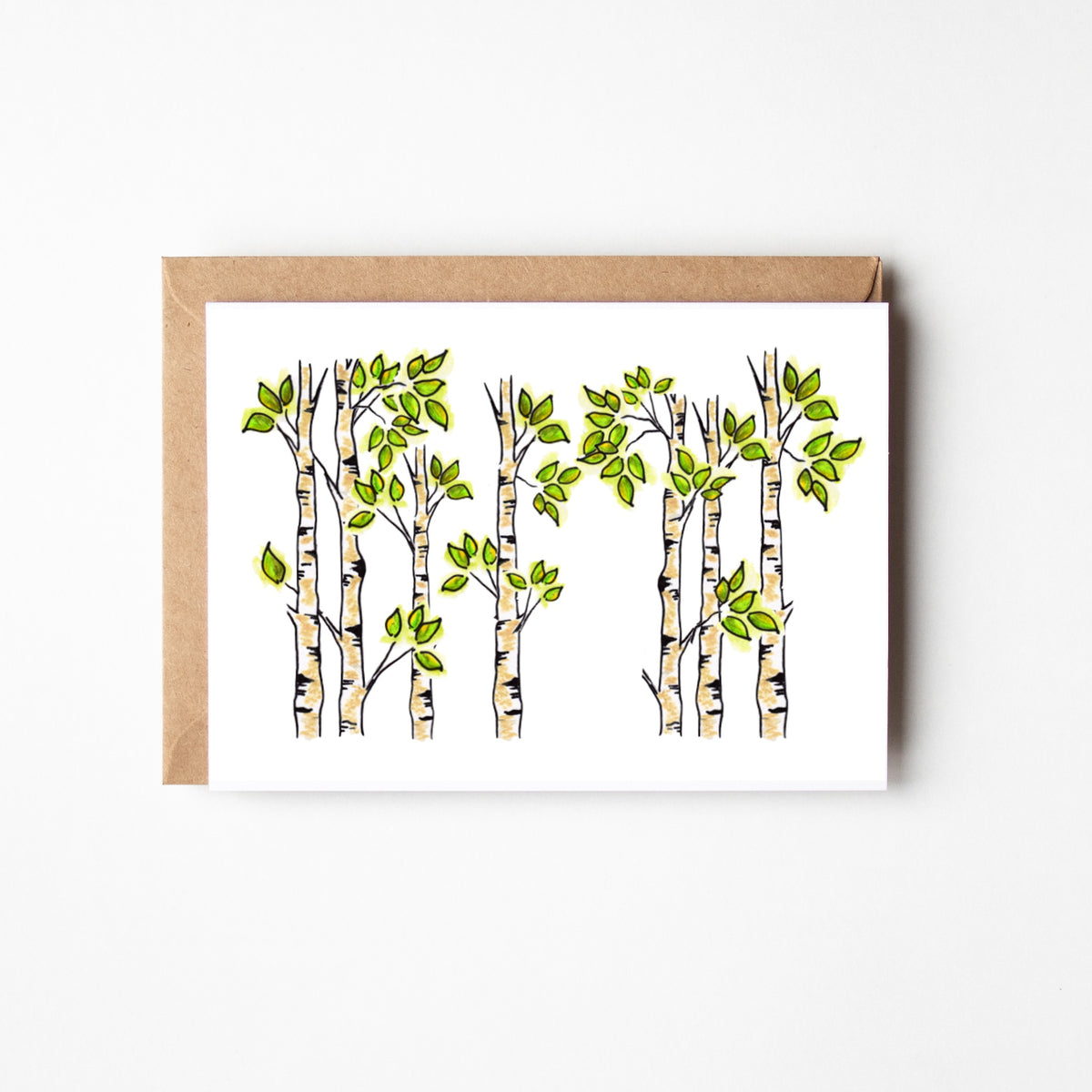 A white greeting card featuring an illustration of birch trees with green leaves, shown with a brown kraft envelope on a light gray background.