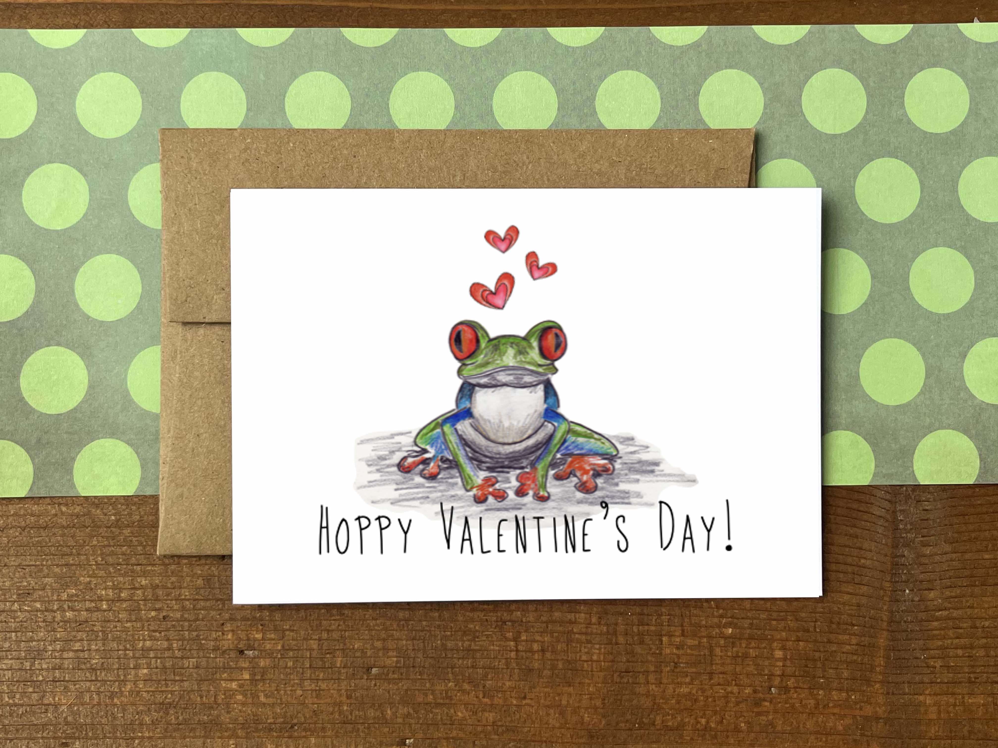 A note card with an illustration of a tree frog and red hearts with the message "Hoppy Valentine's Day!"